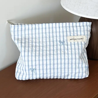 Bolsa de tecido riscada azul e branca com etiqueta e bordados ao lado de lâmpada.