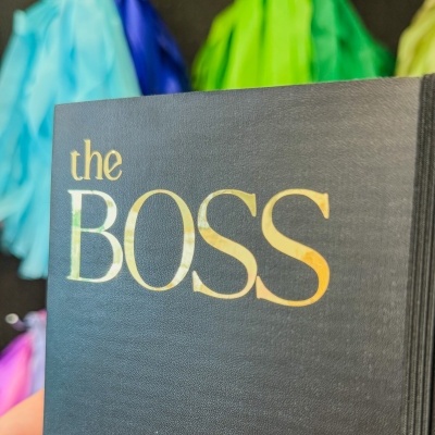 Livro preto com título dourado 'the BOSS' e fundo colorido desfocado