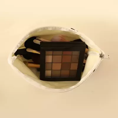 Bolsa branca aberta com estojo de sombras e pincéis de maquilhagem