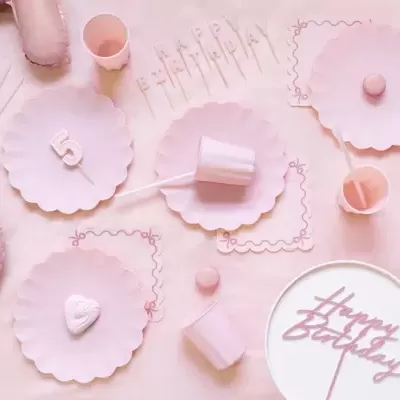 Decoração de festa cor-de-rosa com pratos, copos, balões, palhinhas e bolo com texto Happy Birthday.