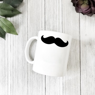Caneca branca com bigode preto sobre mesa de madeira clara