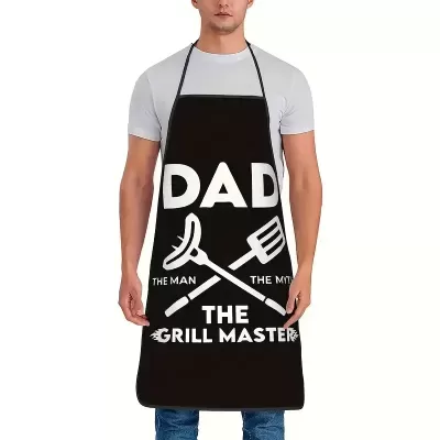 Avental preto com texto branco 'DAD THE MAN THE MYTH THE GRILL MASTER' e gráficos de salsicha e espátula.