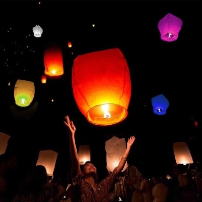 Luzes lanternas de papel coloridas flutuando no céu à noite com pessoa a acenar