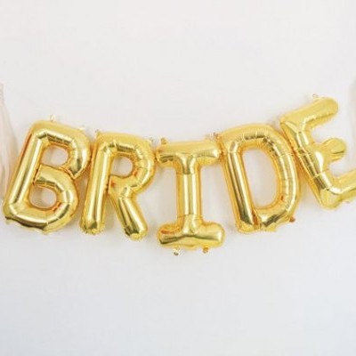 Balões dourados com a palavra BRIDE pendurados numa corda branca com pompons