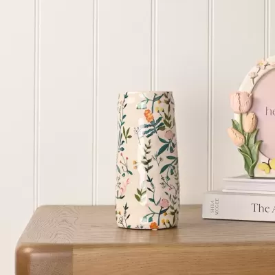 Vaso de cerâmica floral sobre mesa de madeira com livros e porta-retrato decorativo ao lado