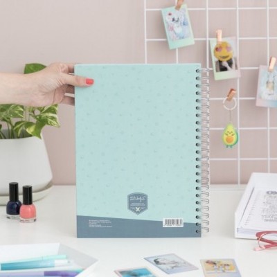 Caderno azul claro de espiral com padrão de pontos e selo cinzento.