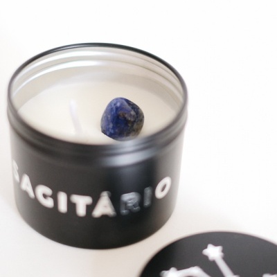Vela em recipiente preto com palavra SAGITÁRIO e pedra azul no centro da cera
