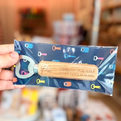 Abridor de garrafas com cabo de madeira gravado e embalagem com fundo azul e chaves coloridas.