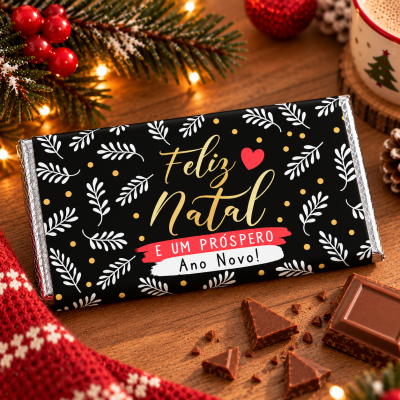 Barra de chocolate com embalagem natalícia preta e decorada com texto e folhas brancas.