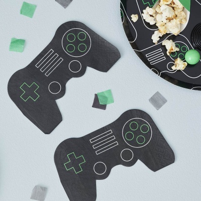 Guardanapos de papel em forma de comandos de videojogos preto com detalhes verdes e brancos sobre mesa cinza com confetes e prato de pipocas