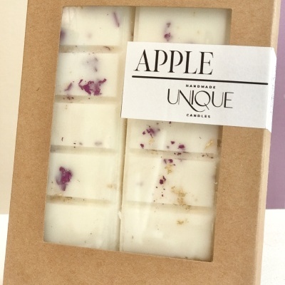 Bloco de cera branca com pedaços roxos em caixa de cartão castanho com tampa transparente e etiqueta branca com texto APPLE.