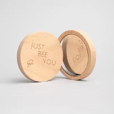 Espelho compacto redondo em madeira clara com texto gravado 'JUST BEE YOU'