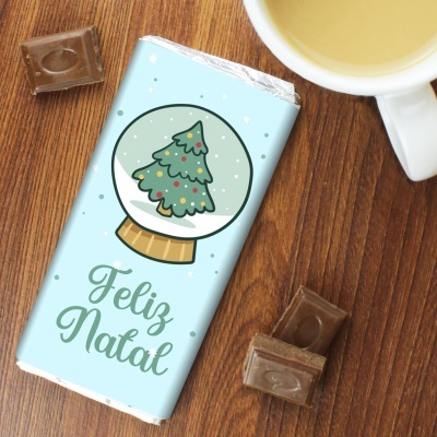 Barra de chocolate embrulhada azul claro com desenho de bola de neve e árvore de Natal e texto Feliz Natal