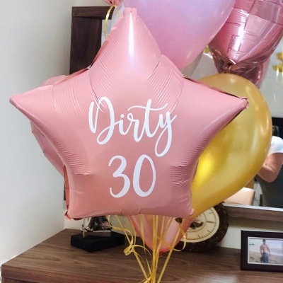 Balões metálicos coloridos decorativos com texto 'Dirty 30' e balões coloridos sobre móvel de madeira