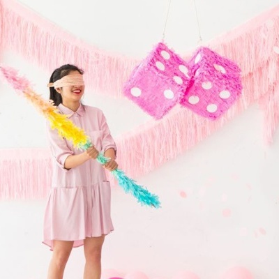 Mulher cega com taco de penas a tentar acertar dois dados cor-de-rosa grandes com pontos brancos suspensos