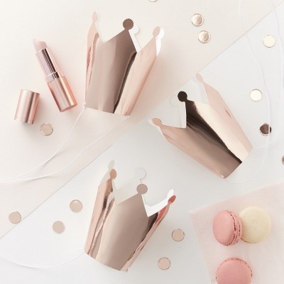 Chapéus metálicos cor de rosa em formato de coroa, batom e macarons sobre fundo claro