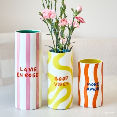 Três vasos cerâmicos coloridos com textos decorativos e flores cor-de-rosa no vaso do meio