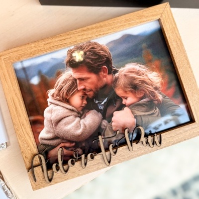 Moldura de madeira clara com fotografia e letras decorativas 'Adoro-te pai'.