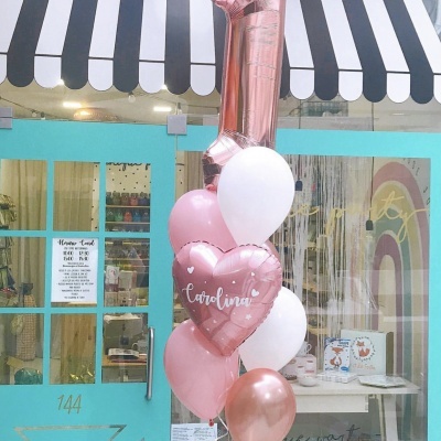 Balões metalizados e brancos juntos em frente a porta azul-turquesa de uma loja