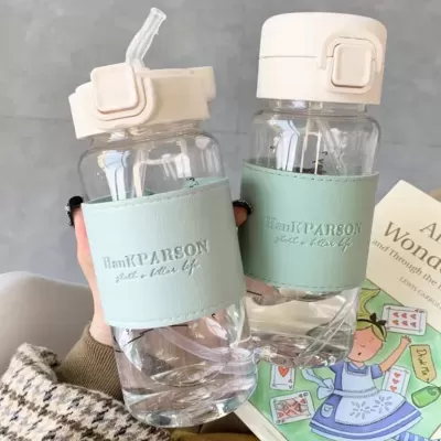 Duas garrafas de água transparentes com faixas verdes e tampas bege sobre mesa cinzenta com livros ao lado