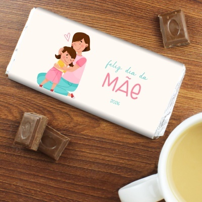 Barra de chocolate com embalagem de dia da mãe e pedaços de chocolate sobre mesa de madeira.