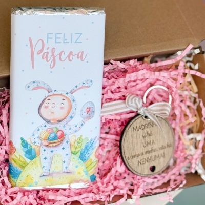 Barra de chocolate decorada com coelhinho e texto Feliz Páscoa junto de chaveiro de madeira com mensagem especial dentro de caixa com papel picado rosa