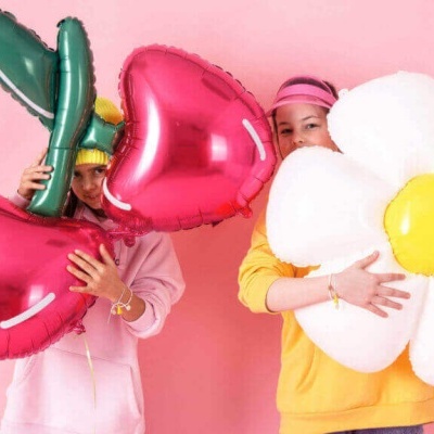 Pessoas segurando balões grandes em forma de cereja, folha e flor contra fundo rosa.
