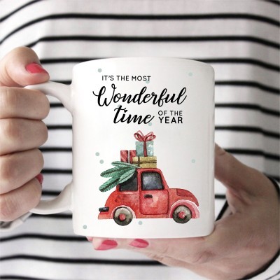 Caneca branca com design natalício e texto em inglês, segurada por pessoa vestindo camisa às riscas pretas e brancas