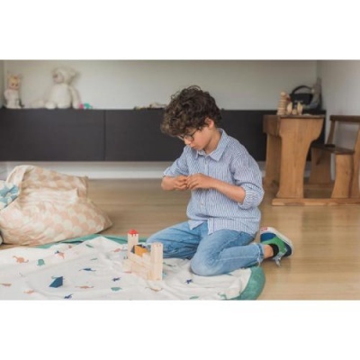 Criança a brincar com bloco de madeira numa manta com padrões coloridos no chão