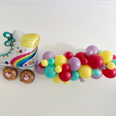 Patim em linha branco com detalhes coloridos e rodas com formato de donuts, junto a um conjunto de balões coloridos num fundo branco