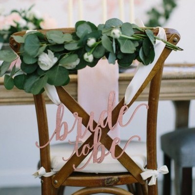 Cadeira decorada com folhas, flores e placa 'bride to be'