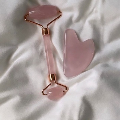 Massageador facial e pedra de gua sha rosa em tecido branco