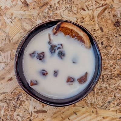 Tigela preta com leite, pedaços escuros e laranja seca numa superfície de madeira
