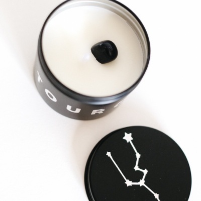 Vela branca em recipiente preto com tampa preta e constelação branca