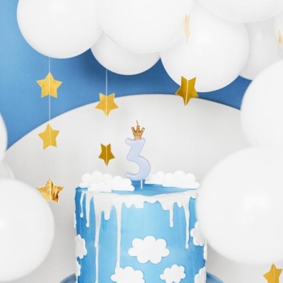 Bolo azul com decoração de nuvens, vela número 3 com coroa, balões brancos e estrelas douradas suspensas.