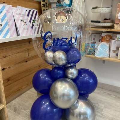 Decoração de balões azul e prateada com balão transparente 'Parabéns Enzo!' em loja