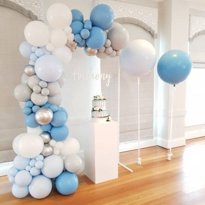 Arco decorativo de balões em azul, branco, cinza e prateado, com bolo em pedestal branco ao lado