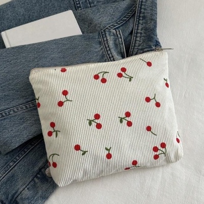 Mala de tecido branco com padrão de cerejas vermelhas sobre ganga azul e livro branco