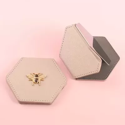 Caixas hexagonais de couro bege com abelha dourada e espelho rosa