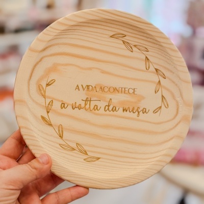 Prato redondo de madeira clara com texto gravado e decoração de folhas