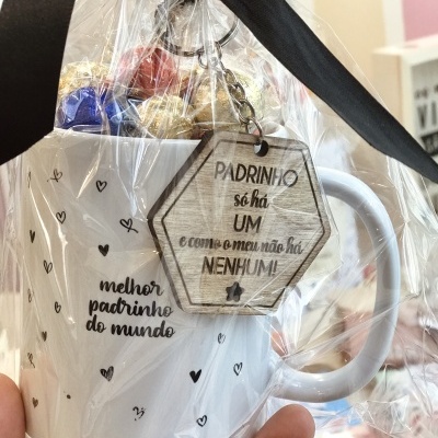 Caneca branca com texto sobre padrinho, decorada com corações, embrulhada com laço e pendente de madeira