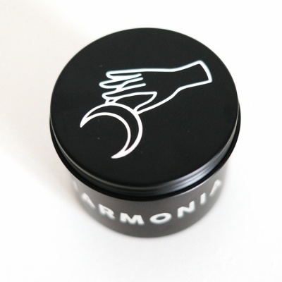 Frasco preto com tampa decorada com mão e meia-lua, texto ARMONIA