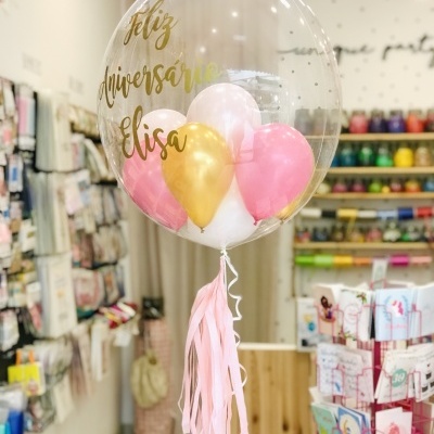 Balão transparente com texto dourado e outros balões coloridos dentro
