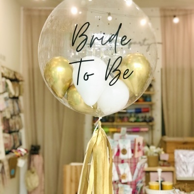 Balão transparente com 'Bride To Be' e balões dourados e brancos no interior em loja
