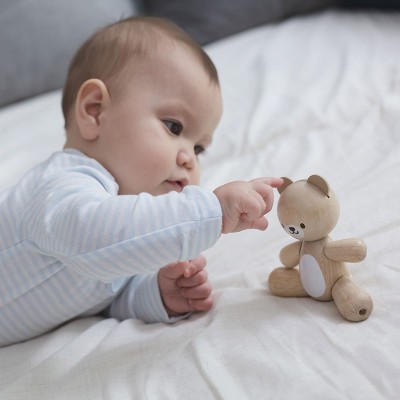 Bebé a tocar ursinho de madeira sentado na cama