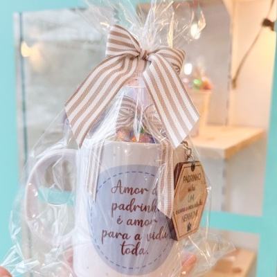 Caneca branca com mensagem em português e laço às riscas, embalada em plástico transparente