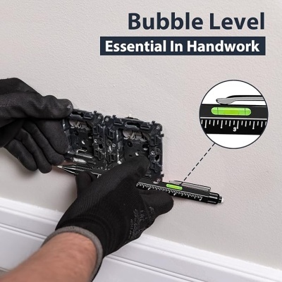 Nível bolha integrado em peça metálica sendo segurada com luvas pretas junto a parede branca