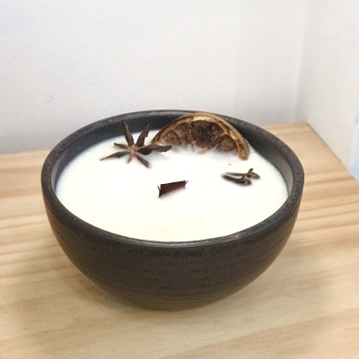 Vela perfumada branca em tigela cerâmica preta com especiarias e laranja seca