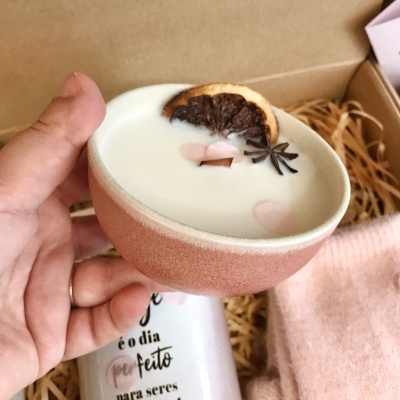 Vela artesanal branca em recipiente cerâmico rosa claro com decoração de laranja seca e anis
