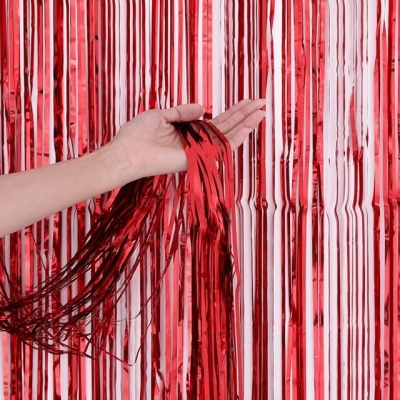 Cortina decorativa metálica vermelha com franjas sendo segurada por uma mão